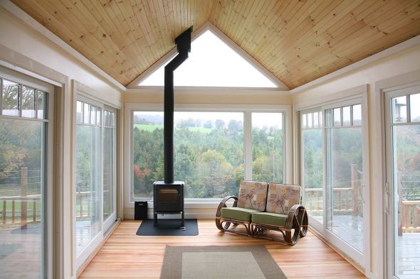 A large living space with a wood stove, couch and green energy efficient windows on all sides looking over hills in Central Vermont