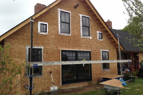 House during home remodeling project with siding removed and new green windows installed