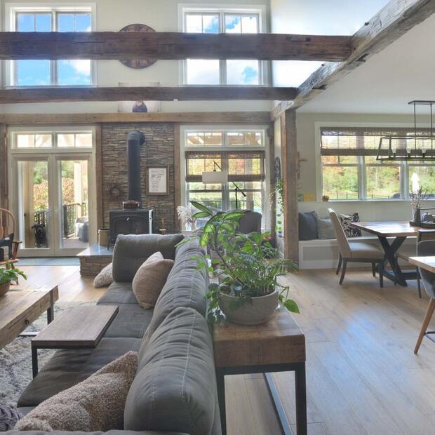 sideview of living room with grey couch, woodstove, and large windows