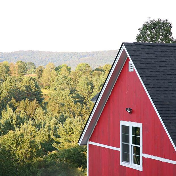 red barn with black roof overlooking a lush green forest and rolling hills