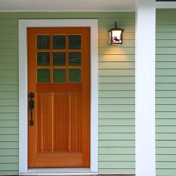 wooden front door with glass panels on a green house with a cozy porch light