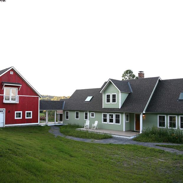 scenic farmhouse with a green main house and red barn on a grassy hill