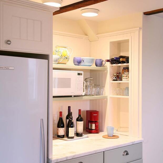 warm kitchen space with a marble countertop, microwave, and neatly arranged mugs, bowls, and wine bottles.