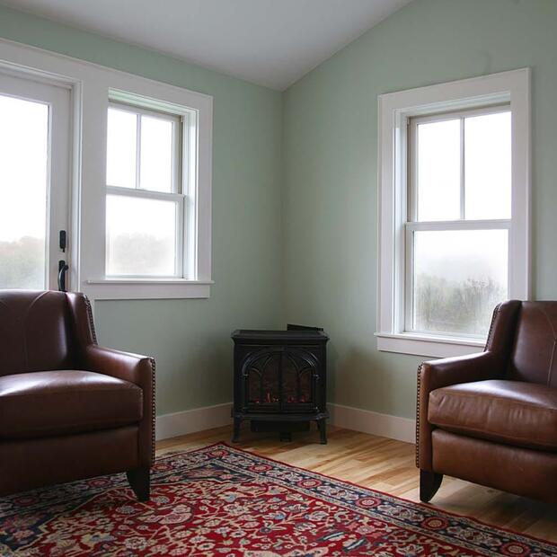 sitting area with two brown leather chairs, a woodstove, and large windows