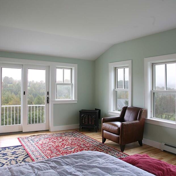 primary bedroom with large windows, a balcony, and cozy leather chairs