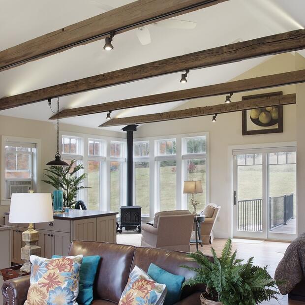 living room with exposed beams, a cozy wood stove, and large windows