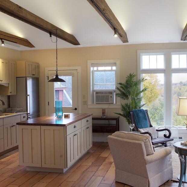 open-concept kitchen and living area with wood beams and a cozy woodstove.