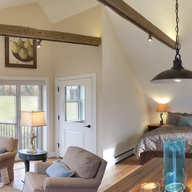 open loft space with a kitchen, living area, and bedroom, all under vaulted wooden beams