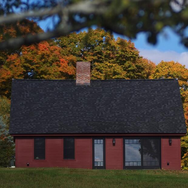 red vermont home with a steep black roof and scenic fall foliage in the background