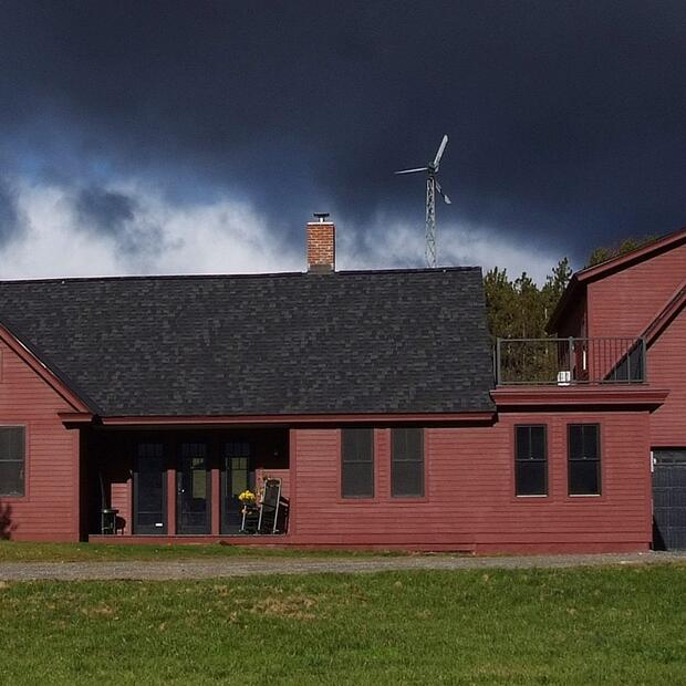 red vermont home with a black roof and a wind turbine, set against a dramatic stormy sky