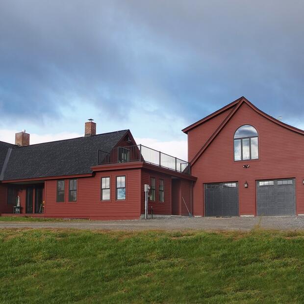 expansive red farmhouse with black garage doors and a rooftop deck under a cloudy sky