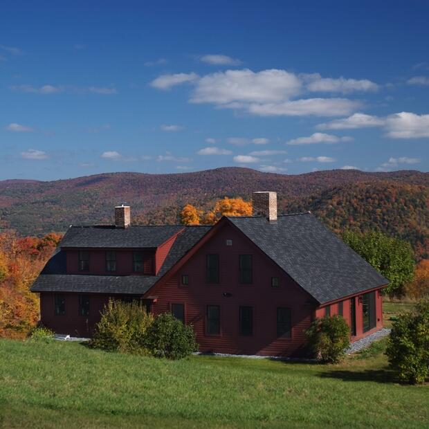 red vermont home nestled in rolling hills with vibrant fall foliage and mountain views