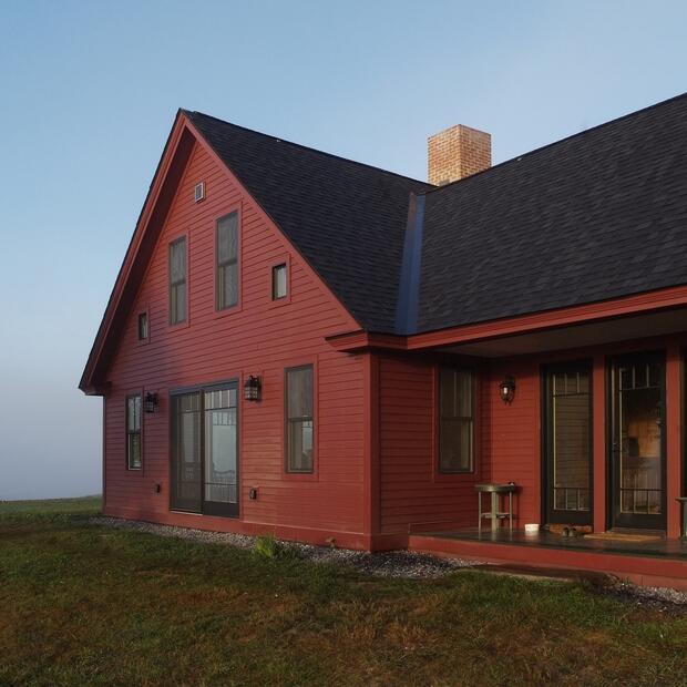 red farmhouse with a covered porch and black-framed doors on a foggy morning