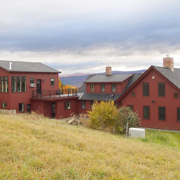 red vermont home with a black roof, rooftop deck, and scenic fall countryside views