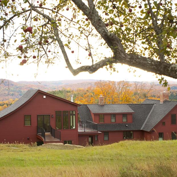 red farmhouse framed by an apple tree with autumn mountains in the background