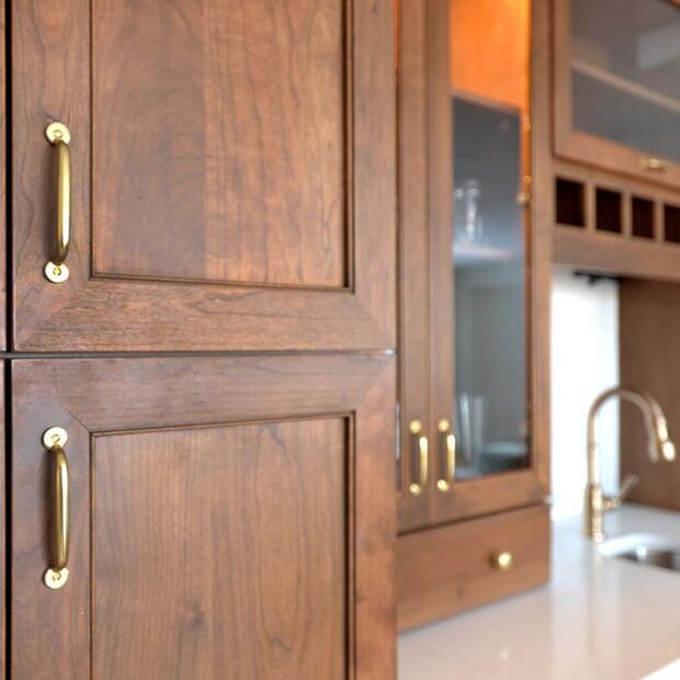 wet bar with warm wood tones, brass hardware, and glass cabinets