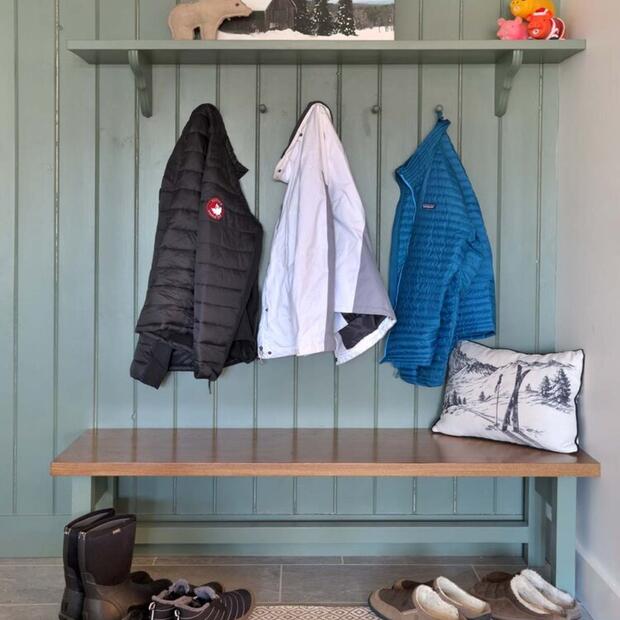 cozy mudroom featuring a green paneled wall, jackets, and a decorative shelf